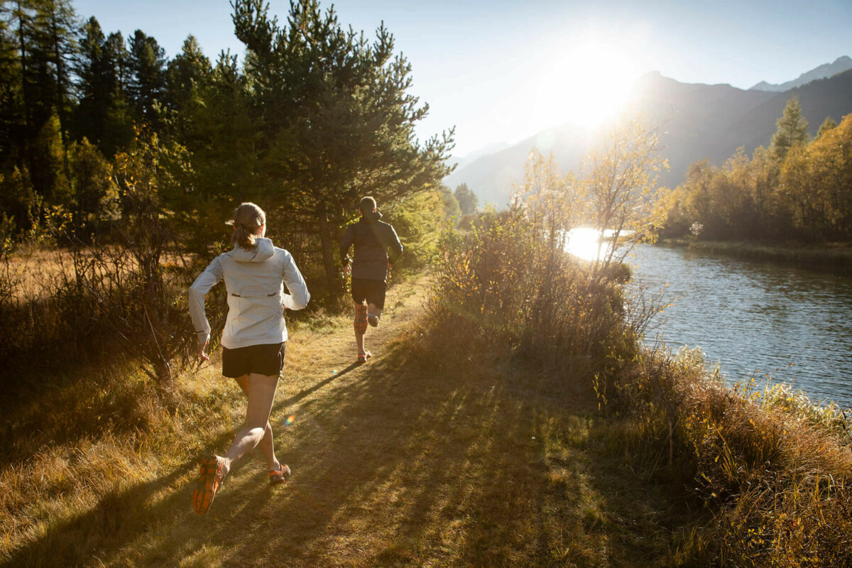 A man and woman running by a river surrounded by mountains