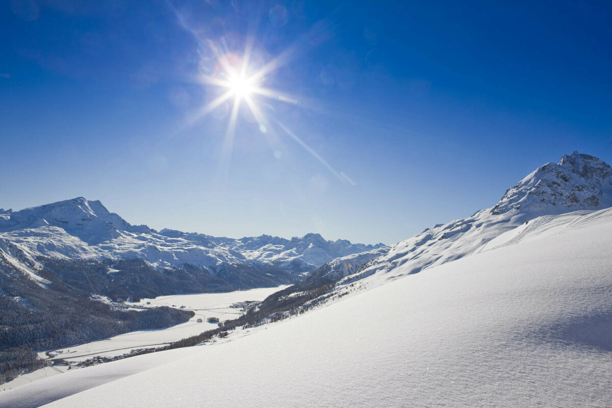 Blick auf verschneite Berghänge mit Sonnenschein und blauem Himmel