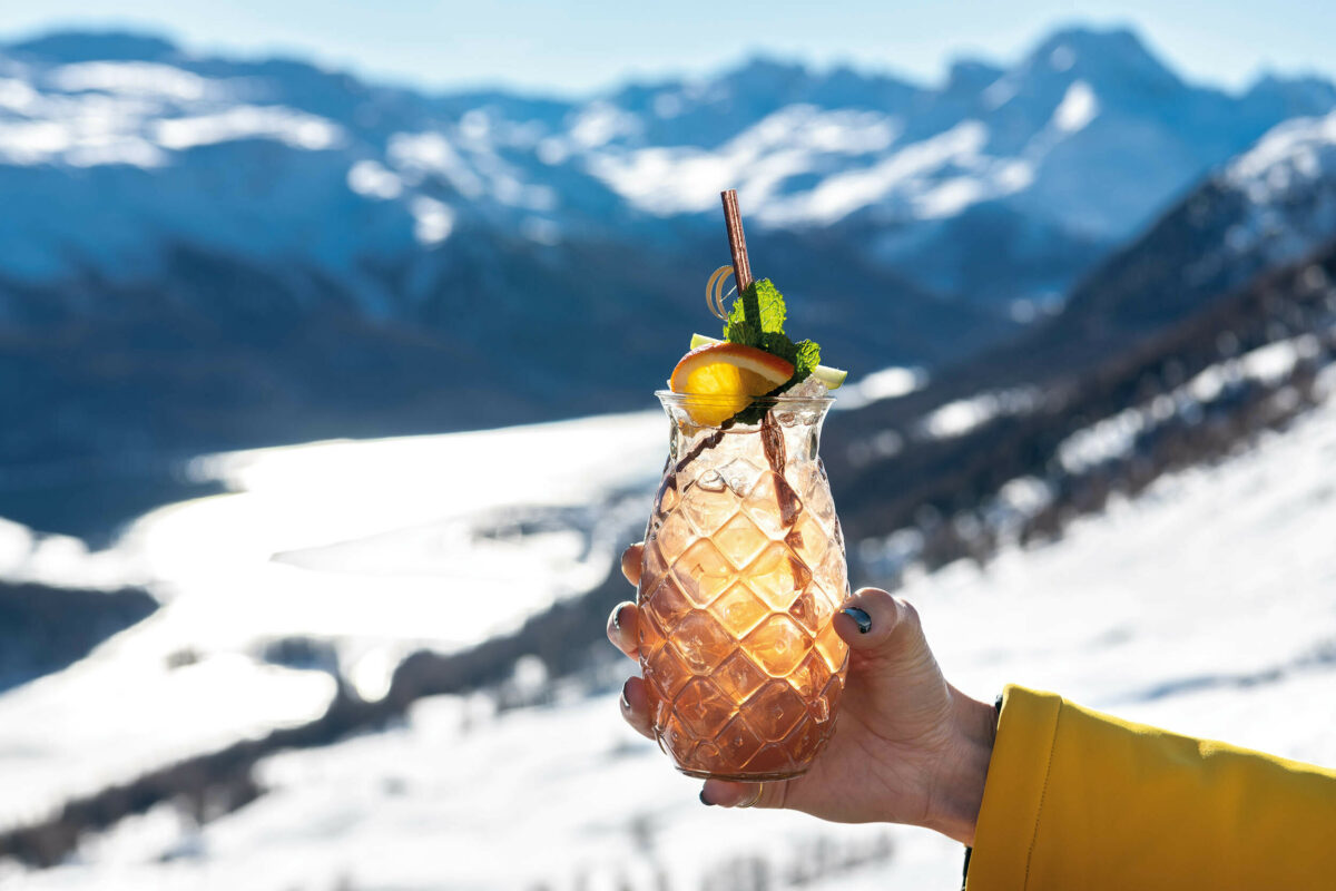 Someone holding up a cocktail in front of snowy mountains