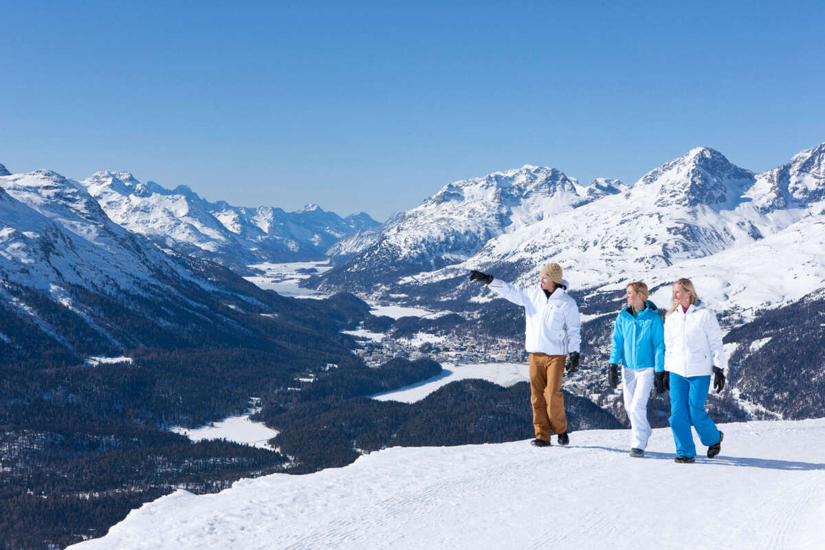 Drei Wanderer auf einem verschneiten Berg mit Blick auf das Engadin