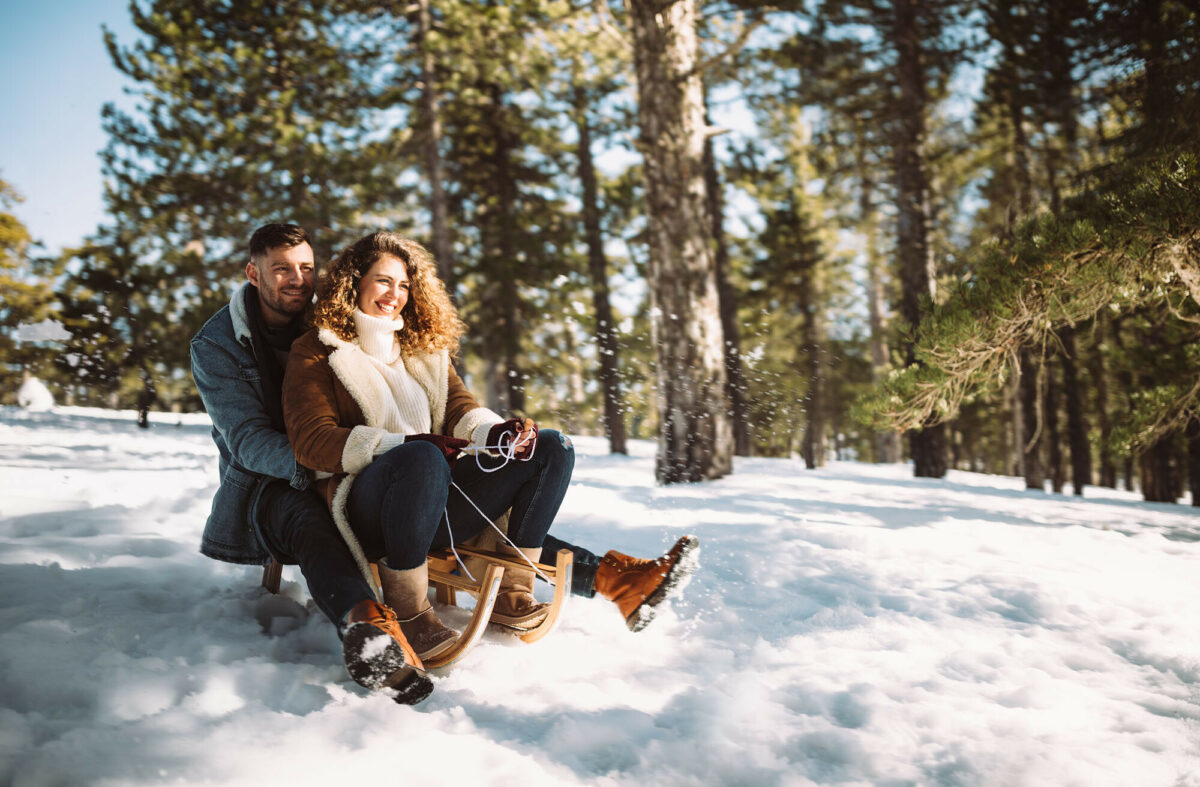 Fröhliches Paar auf Schlitten im verschneiten Wald