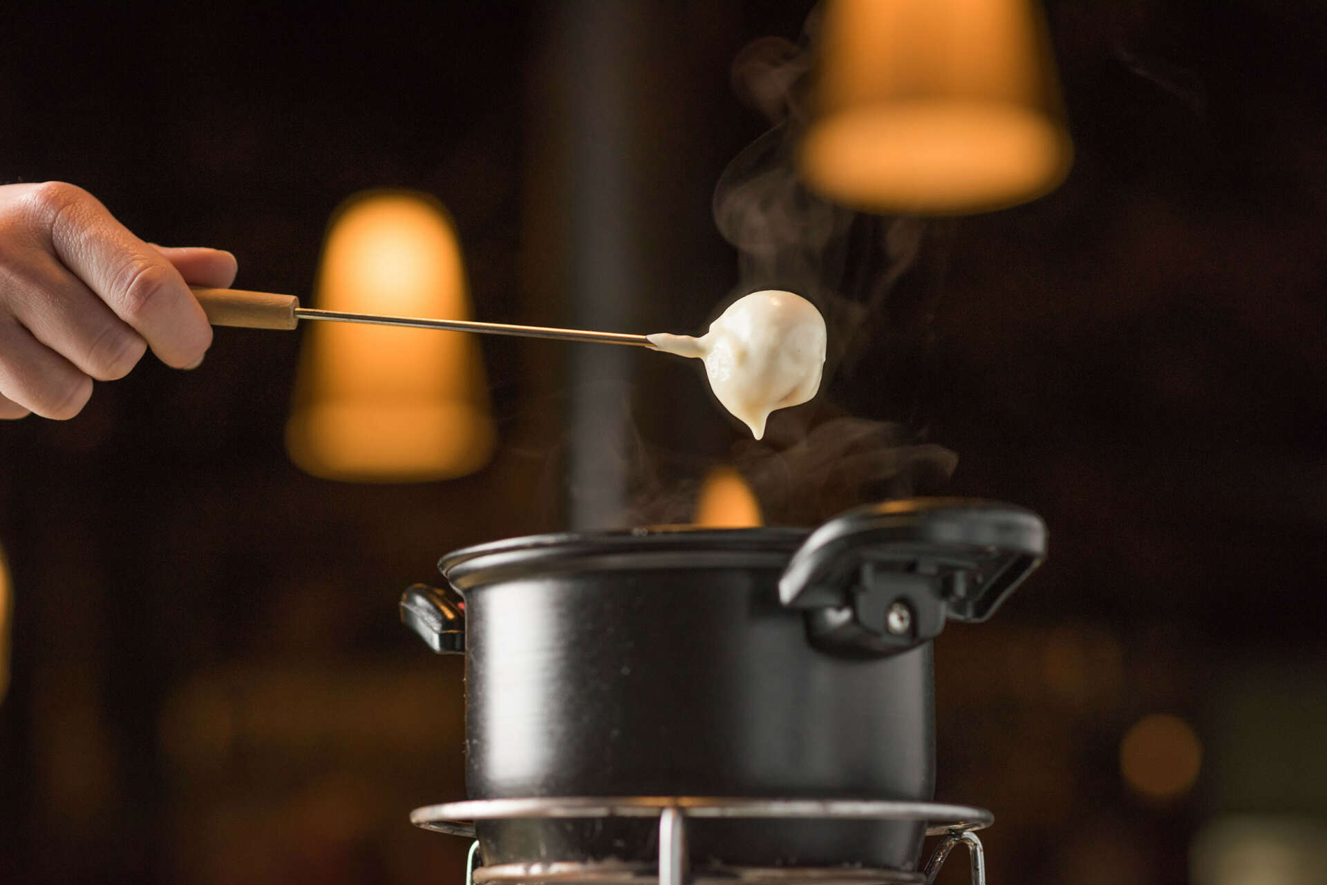 Someone dipping their fork into a cheese fondue pot