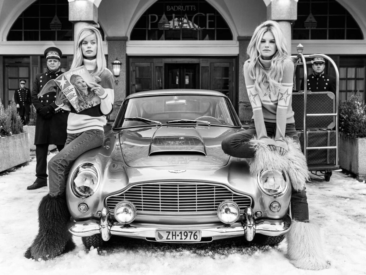 Models leaning on vintage car in front of a luxury hotel