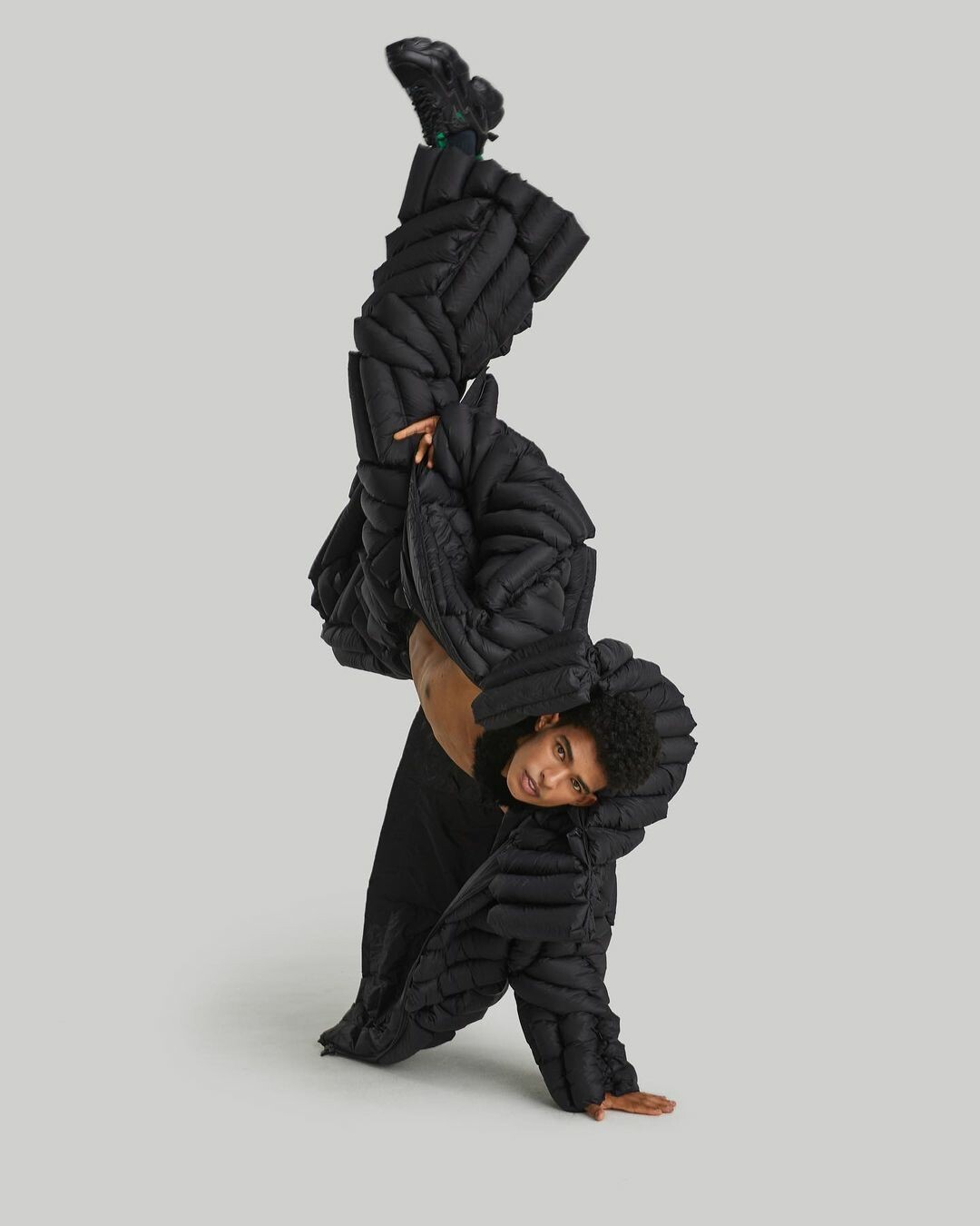 Male model balancing on one hand in black puffer suit